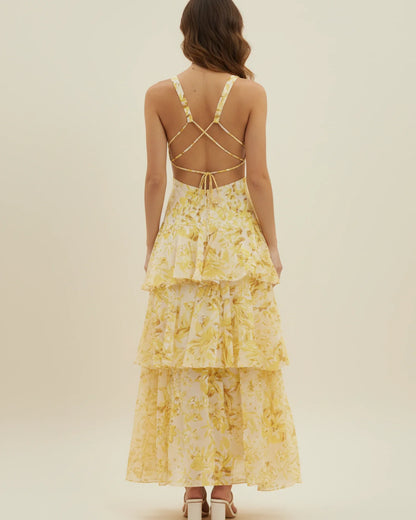 Yellow - A woman models a formal plunging V-neck maxi dress featuring a vibrant teal and navy abstract print and a flowing tiered skirt.