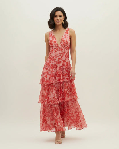 Red - A woman models a formal plunging V-neck maxi dress featuring a vibrant teal and navy abstract print and a flowing tiered skirt.