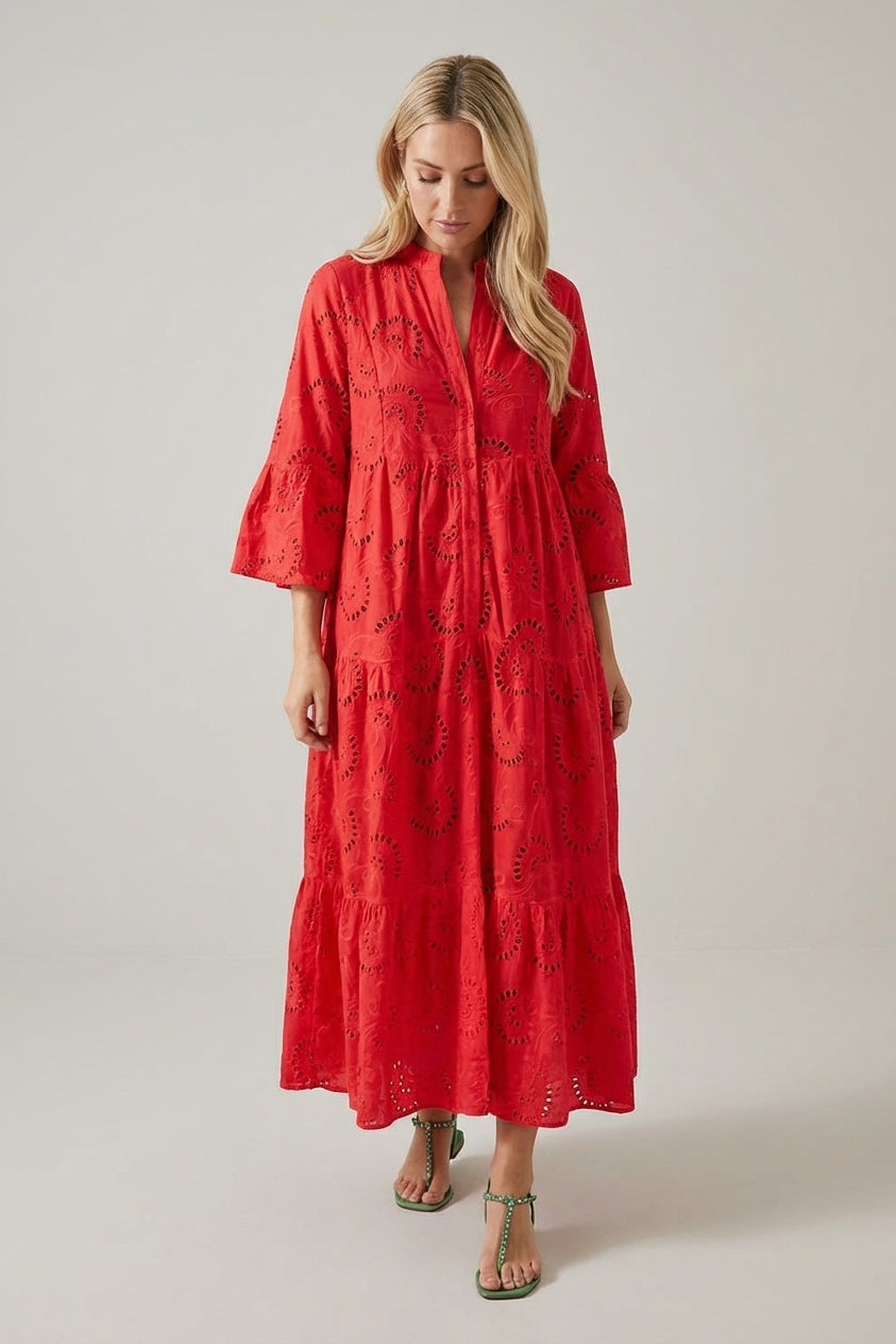 Red - A woman wearing a white, tiered broderie anglaise maxi dress with three-quarter bell sleeves, a split v-neckline, and a relaxed silhouette, paired with green flat sandals.