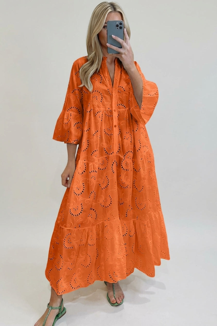 Orange - A woman wearing a white, tiered broderie anglaise maxi dress with three-quarter bell sleeves, a split v-neckline, and a relaxed silhouette, paired with green flat sandals.