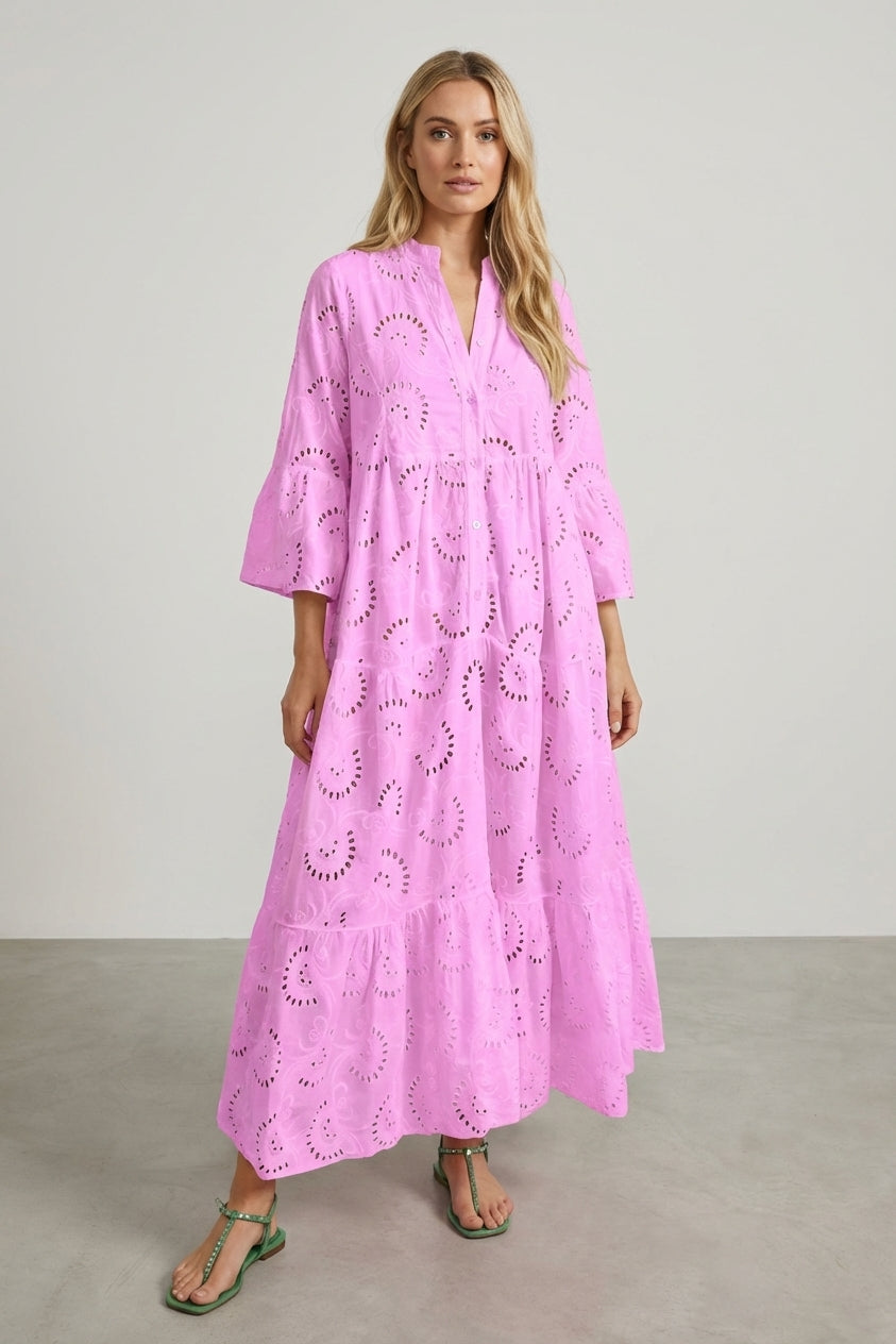 Light Pink - A woman wearing a white, tiered broderie anglaise maxi dress with three-quarter bell sleeves, a split v-neckline, and a relaxed silhouette, paired with green flat sandals.