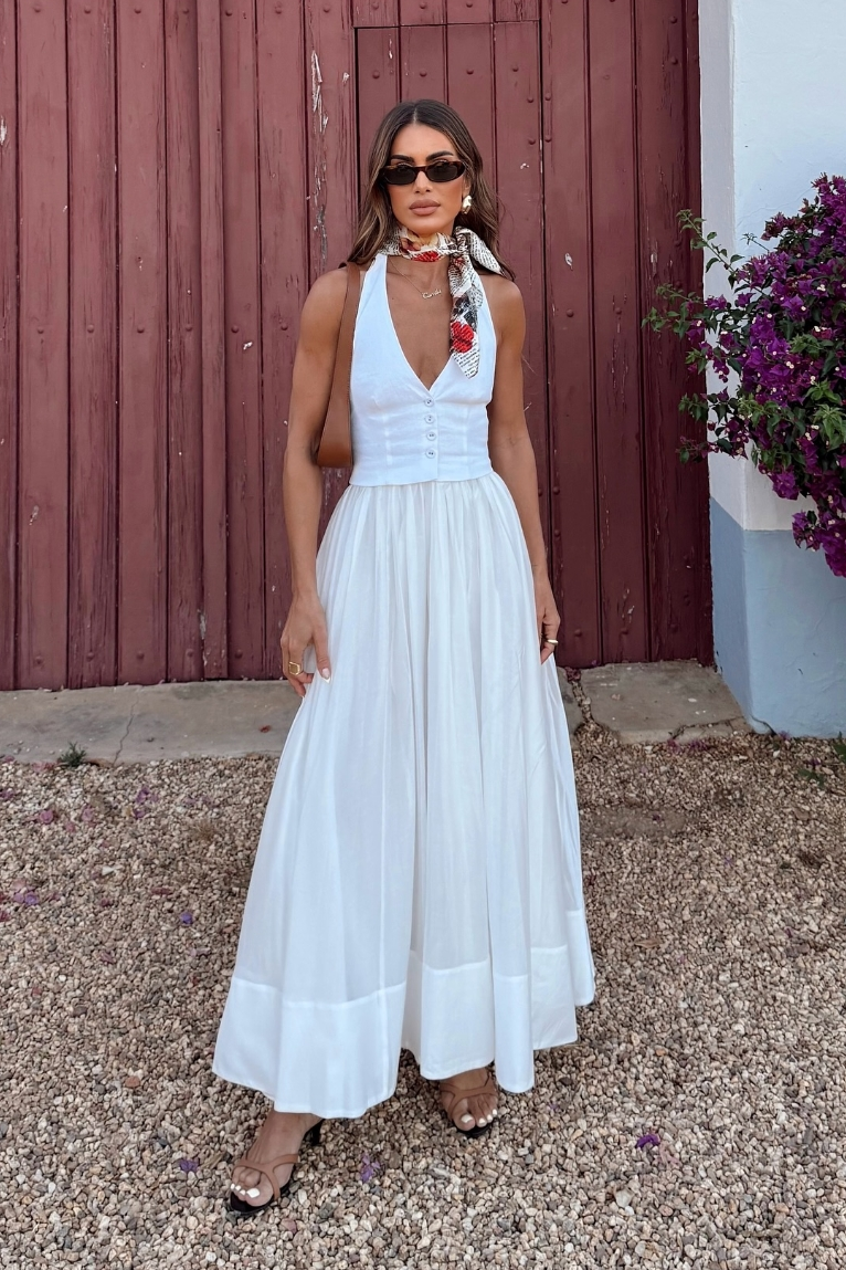 White - A woman wearing a white sleeveless maxi dress with a tailored button-front bodice and a voluminous gathered skirt, styled with a patterned silk scarf and sunglasses.