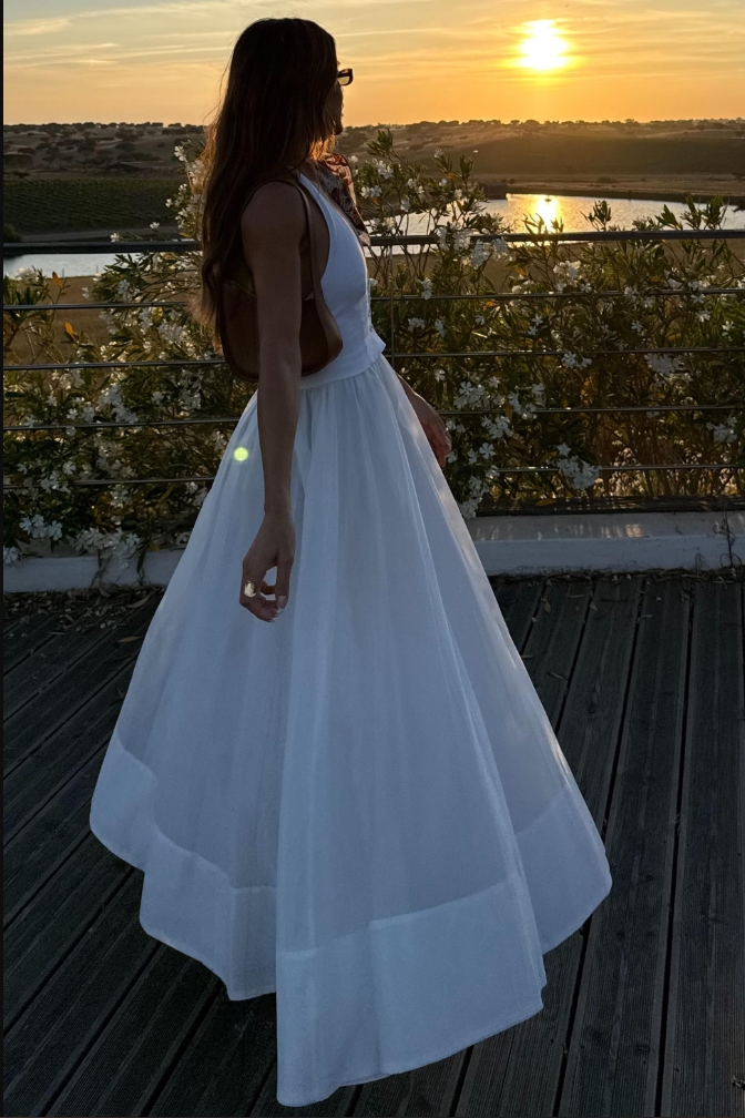 White - A woman wearing a white sleeveless maxi dress with a tailored button-front bodice and a voluminous gathered skirt, styled with a patterned silk scarf and sunglasses.