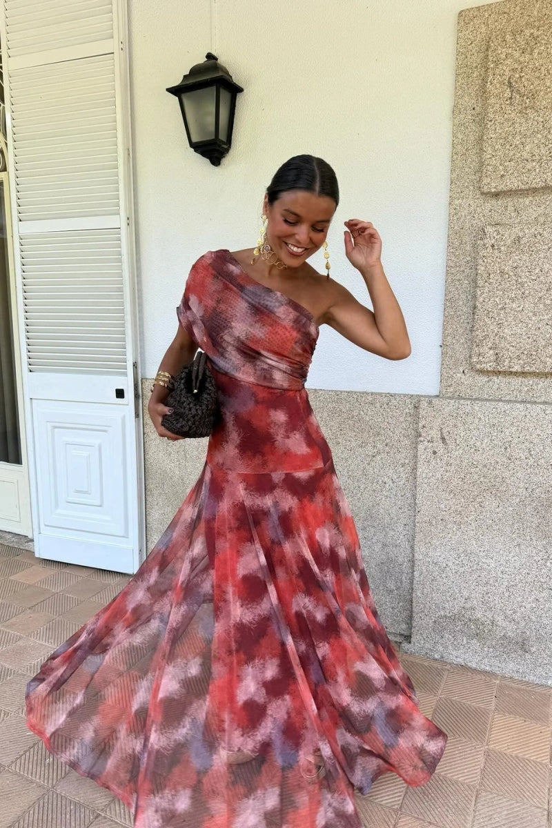 Red - A woman wearing a one-shoulder maxi dress with a red and purple watercolor print, featuring a ruched bodice and a flowing chiffon skirt.