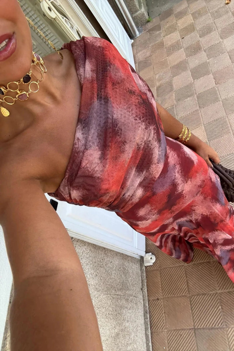 Red - A woman wearing a one-shoulder maxi dress with a red and purple watercolor print, featuring a ruched bodice and a flowing chiffon skirt.