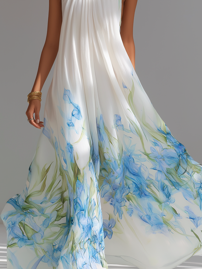 White Printed - A model wears a sleeveless, high halter neck maxi dress made of flowing white chiffon with a blue and green watercolour floral print cascading down the voluminous skirt.
