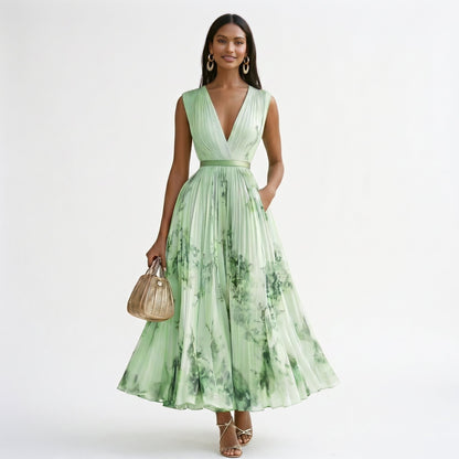 Green - A woman wearing a light blue long-sleeve maxi dress with a deep V-neck, pleated bodice and skirt, featuring a blue and grey watercolour floral print.