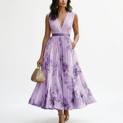 Purple - A woman wearing a light blue long-sleeve maxi dress with a deep V-neck, pleated bodice and skirt, featuring a blue and grey watercolour floral print.